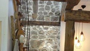 Una escalera de madera con pared de piedra, barandilla metálica y una lámpara colgante.