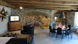Una habitación de paredes de piedra con chimenea, una mesa de comedor para cuatro personas y un televisor sobre un mueble de madera.