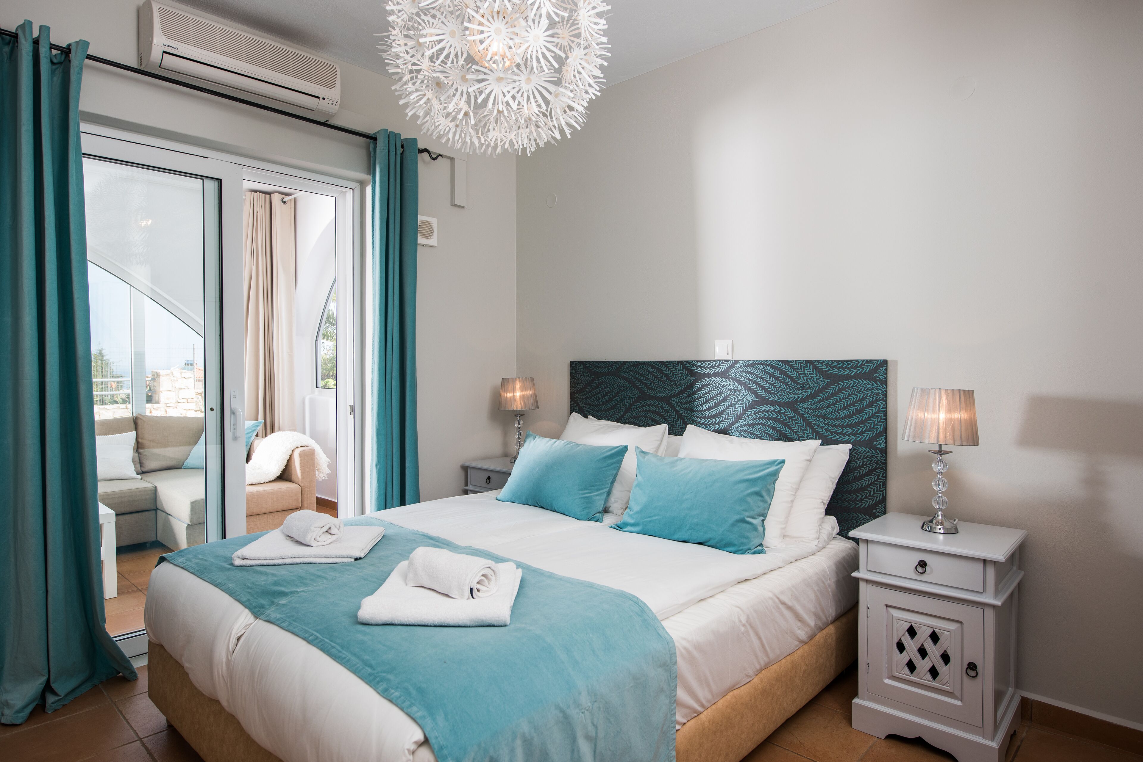 A hotel room with a bed, a nightstand, a lamp, a ceiling fan, and a view of the outside.