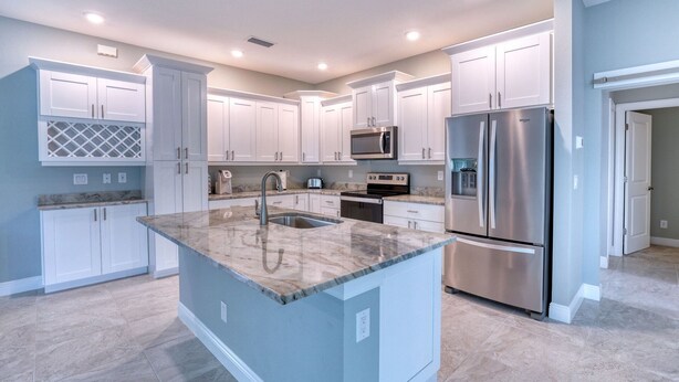 A modern kitchen with white cabinets, stainless steel appliances, and a marble countertop.