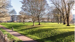 Un parc avec un sentier dallé, des arbres et un bâtiment en arrière-plan.