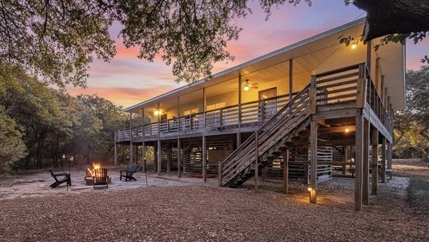 A two-story wooden cabin with a covered porch, outdoor seating, and a fire pit. - Beach Blessing - Southern Shores, 225 to Beach Access, Quiet Area, Hot Tub, Pets OK, Flex Stays (Southern Shores)