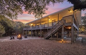 A two-story wooden cabin with a covered porch, outdoor seating, and a fire pit.