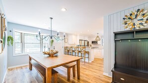 A kitchen with wooden flooring, a dining table, and a large decorative wall piece. - Beach Blessing - Southern Shores, 225 to Beach Access, Quiet Area, Hot Tub, Pets OK, Flex Stays (Southern Shores)