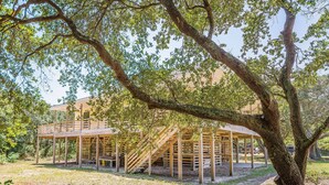 A wooden structure with a staircase leading to a covered area, surrounded by trees. - Beach Blessing - Southern Shores, 225 to Beach Access, Quiet Area, Hot Tub, Pets OK, Flex Stays (Southern Shores)