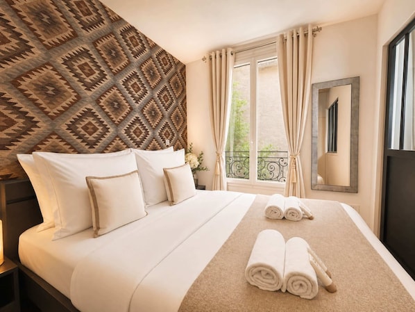 A hotel room with a bed, a window with curtains, a mirror, and a patterned wall.