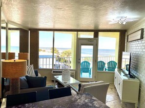 A room with a view of the sea, a dining area, and a TV on a cabinet.