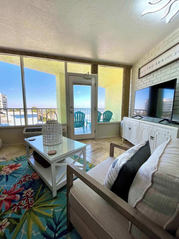 A balcony with a view of the sea, a TV, a white cabinet, and a floral-patterned rug.