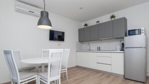 A modern kitchen with white cabinets, a built-in microwave, and a dining area with a round table and white chairs. - Apartments Antonio (Tucepi)