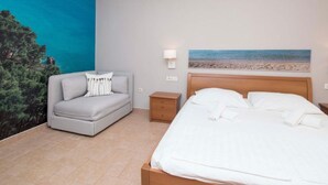 A bedroom with a bed, a grey sofa, a nightstand, and a wall mural of a beach. - Apartments Antonio (Tucepi)