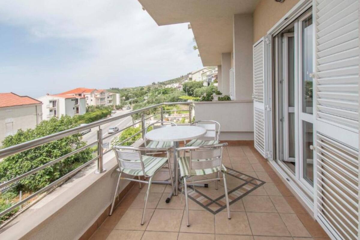 A balcony with a table and chairs, a view of the neighborhood, and a building with shutters.