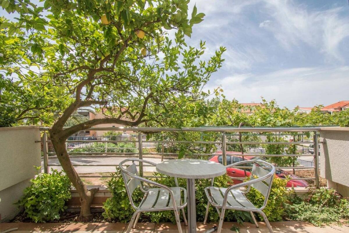 A balcony with a round table and two chairs, surrounded by greenery and a tree.