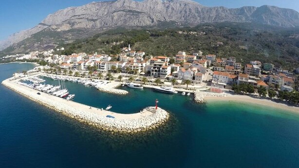 A coastal town with a marina, buildings, and mountains in the background. - Apartments Antonio (Tucepi)