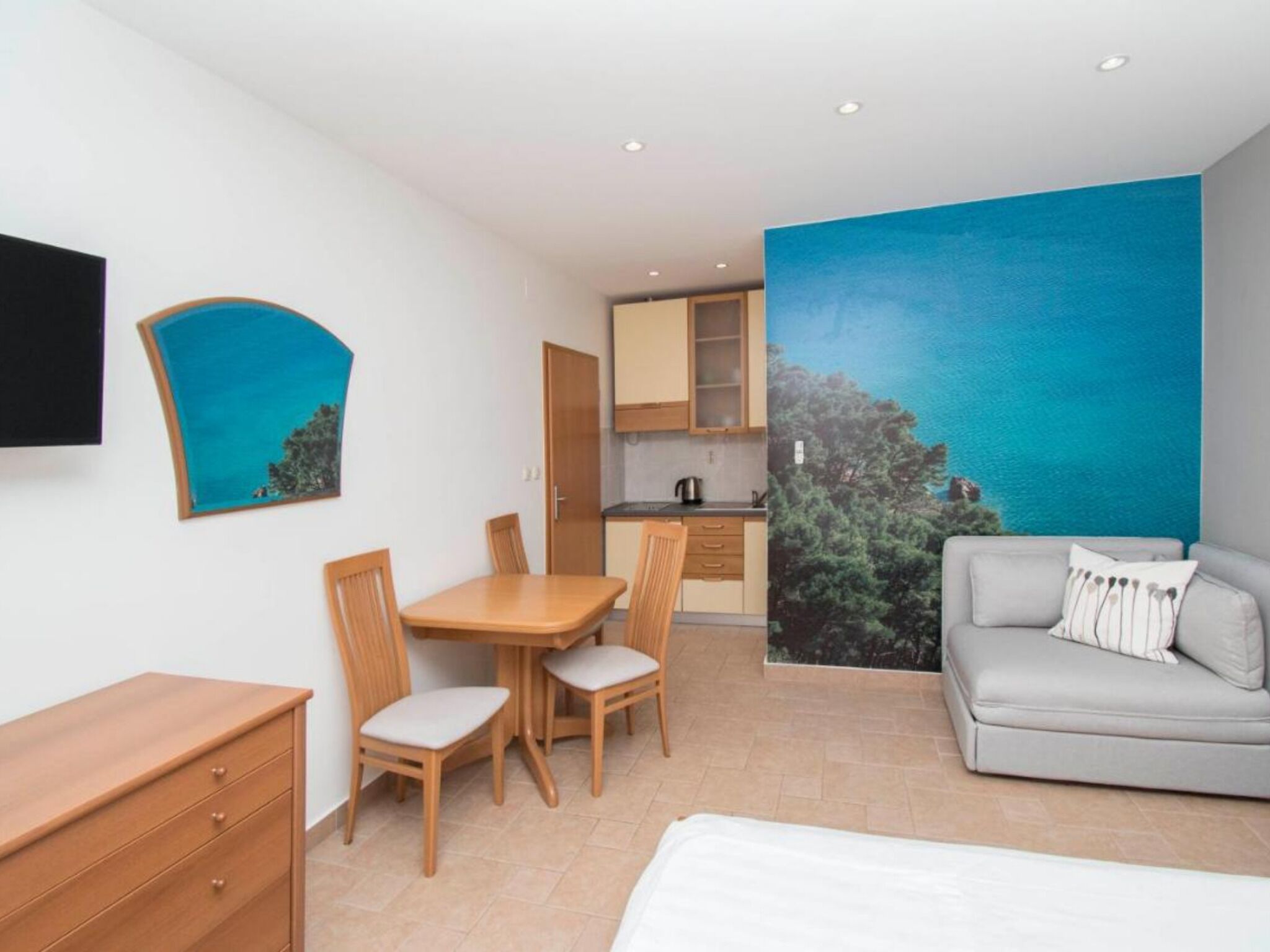 Une pièce comprenant un lit, un bureau, une chaise, un canapé et un tableau représentant un paysage bleu.