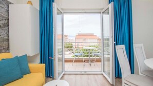 A modern room with a yellow sofa, a small round table, and a balcony with blue curtains. - Apartments Antonio (Tucepi)