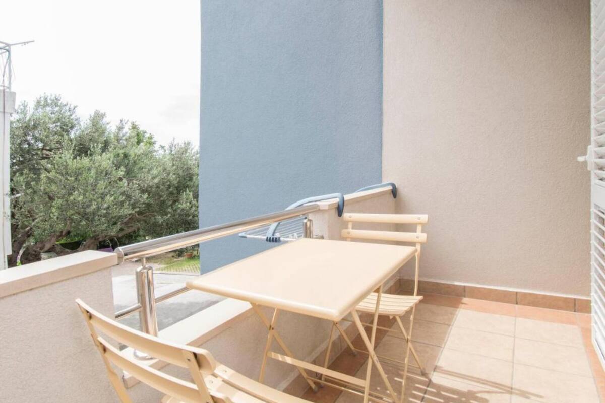 A balcony with a table and chairs, a railing, and a view of trees and a building.