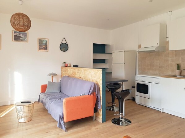 Un espacio habitable compacto con sofá, mesa de comedor, zona de cocina y un taburete pequeño.