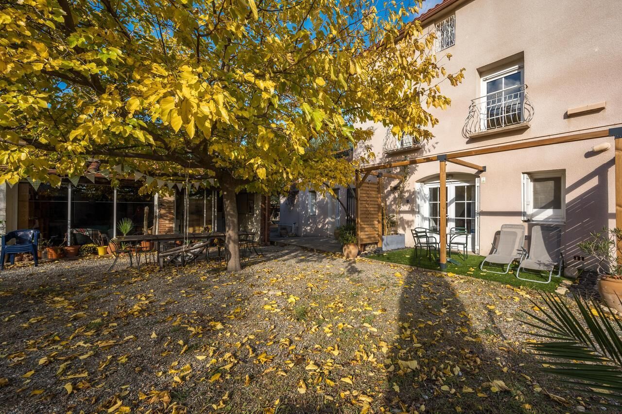 Une cour avec un arbre aux feuilles jaunes, une pergola en bois et un bâtiment doté d’un balcon.