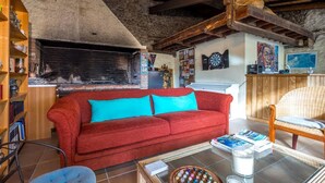 Un salon chaleureux avec une cheminée, un canapé rouge, une table basse avec des livres et une bougie, et une chaise en bois.
