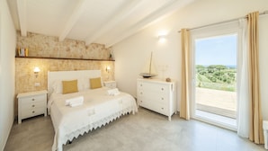 Une chambre à coucher avec un lit, des tables de chevet, une commode et une vue sur l’extérieur.