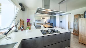 Une cuisine moderne avec un îlot central, un coin repas avec un canapé et un salon équipé d’un téléviseur.