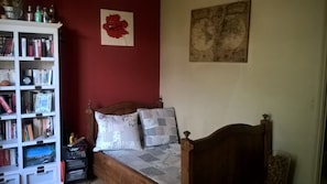 Une chambre avec un lit en bois, une bibliothèque, un tableau représentant une fleur rouge et une carte du monde accrochée au mur.