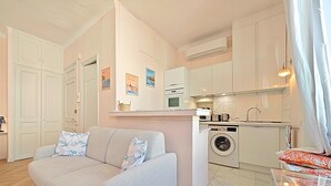 A compact living space with a sofa, a washing machine, and a kitchenette. - Viva Riviera Studio 5 Rue Florian (Cannes)