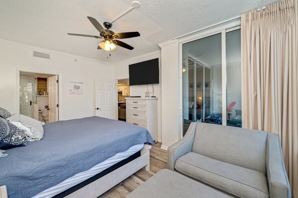 A bedroom with a bed, a ceiling fan, a TV, and a sliding glass door to a balcony.