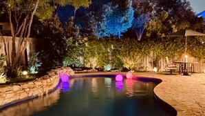 Piscina con borde de piedra, rodeada de árboles y una valla de madera.