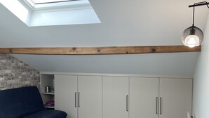 Ein Zimmer mit Oberlicht, Holzbalken, einem dunkelblauen Sofa, weißen Schränken und einer Heizung.