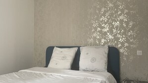 Ein Schlafzimmer mit einem Bett, Kissen, einem Nachttisch und einer Wand mit einem Blumenmuster.