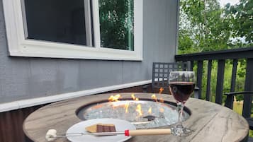 A round wooden table with a built-in fire pit, a plate with a piece of meat, a skewer, and a glass of red wine.