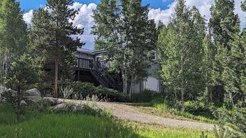 A residential property with a staircase leading to a deck, surrounded by lush greenery and tall trees.
