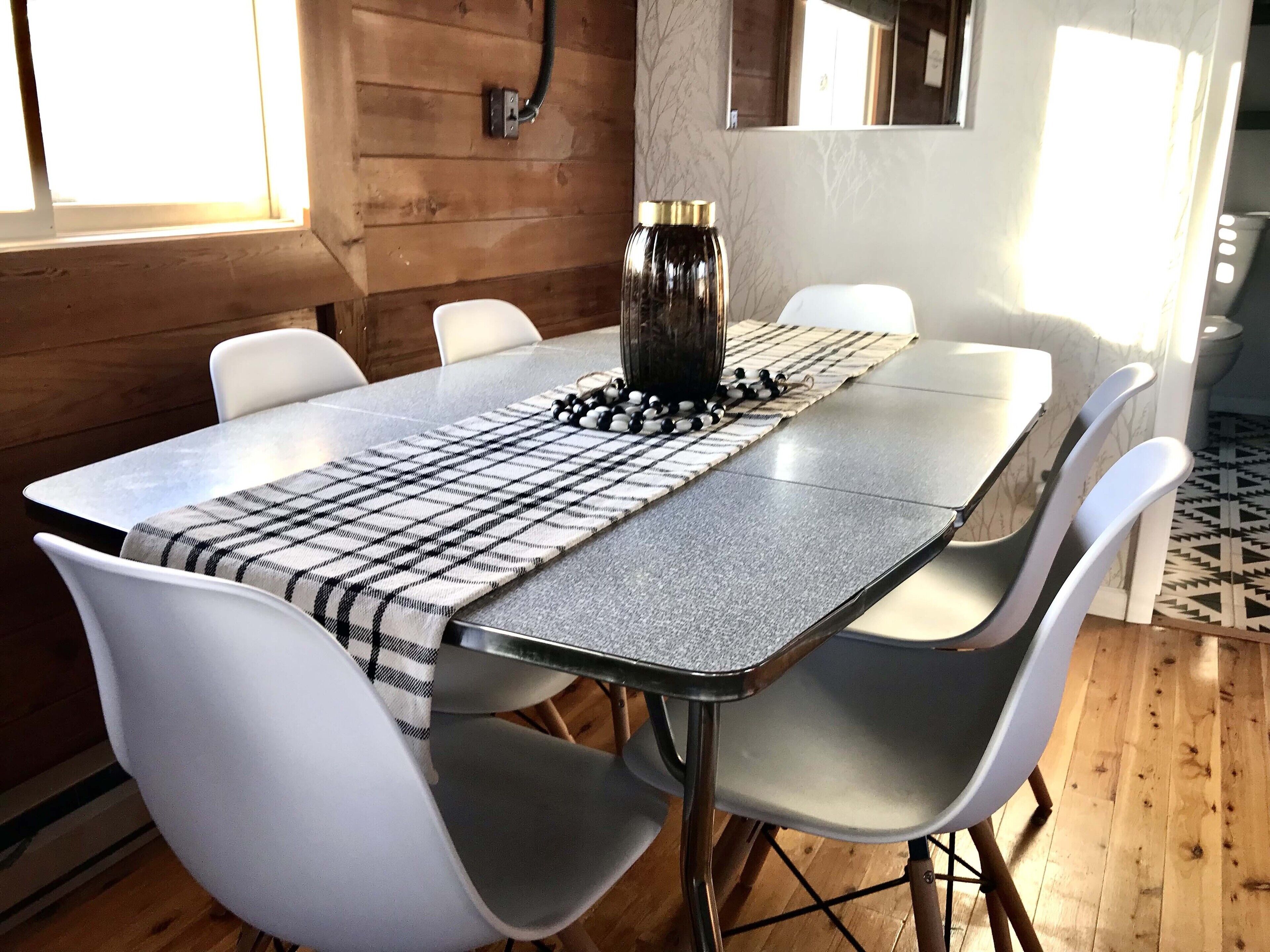 A dining table with a checkered table runner, white chairs, and a decorative centerpiece.