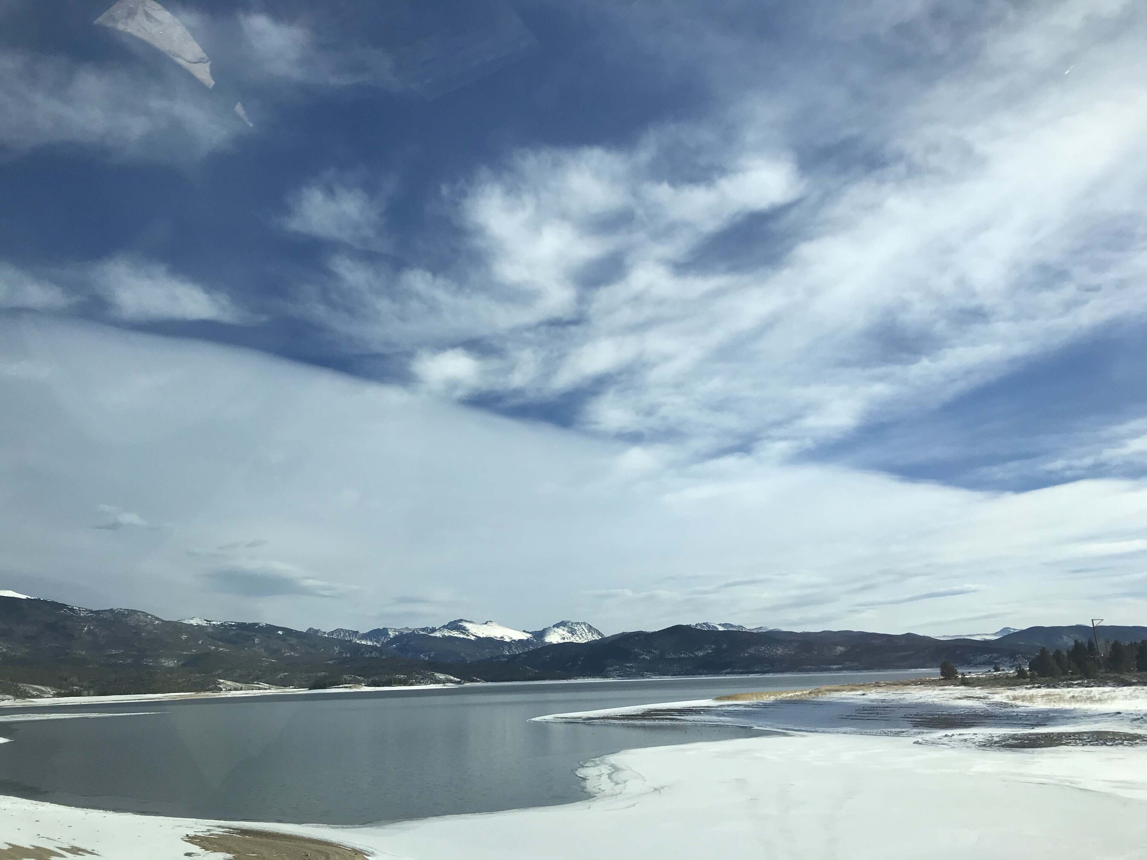 A panoramic view of a lake with snow-covered shores and mountains in the background.