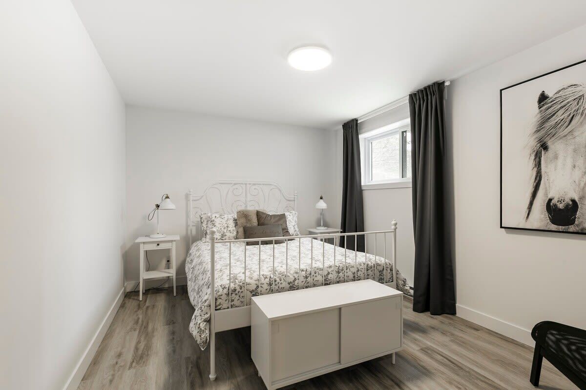 Une chambre à coucher comprenant un lit, des tables de chevet, un banc, une fenêtre avec des rideaux et une œuvre d’art accrochée au mur.
