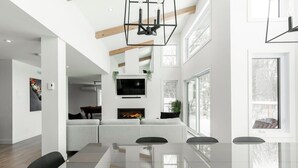 Amplia sala de estar con una mesa de comedor de cristal, una chimenea y un televisor grande.