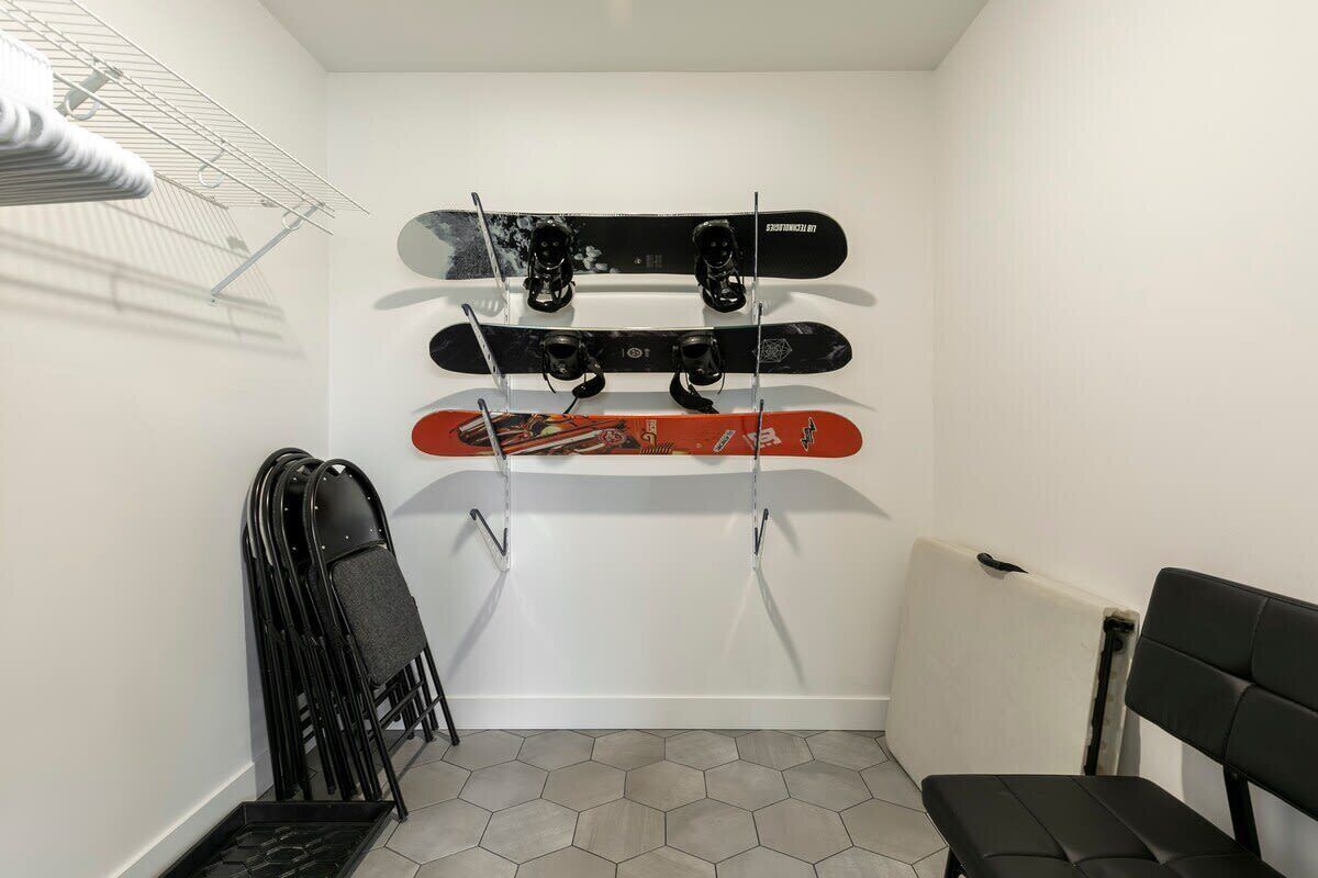 Een hoekzaal met een witte muur, een radiator, een zwarte stoel en een rek met daarin drie ski's.