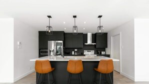Una cocina moderna con una isla central, armarios negros y tres taburetes de bar.