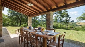 An outdoor dining area with a stone pillar, wooden table, and chairs, overlooking a scenic landscape.