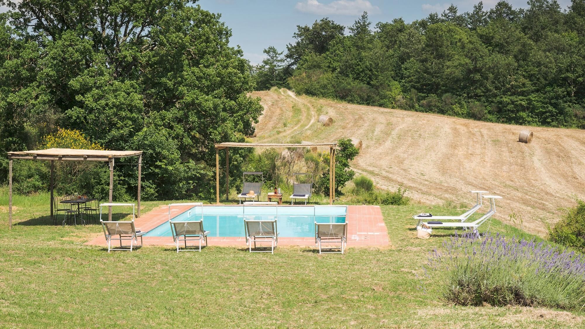 Un espace piscine agrémenté de chaises et d’une pergola, entouré de verdure et dominant un paysage vallonné.