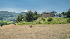 A stone building with a sloped roof, surrounded by a grassy field with hay bales.