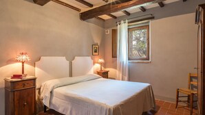 A bedroom with a bed, two bedside tables with lamps, a window with curtains, and a wooden chair.