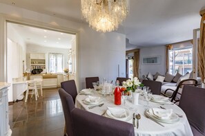 Ein Essbereich mit einer Chandelier, weißen Tischdecken und Blick auf die Küche und das Wohnzimmer.
