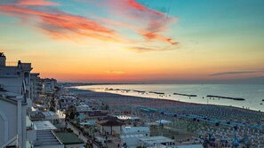 Eine Küstenstadtlandschaft bei Sonnenuntergang mit einem Strand, gesäumt von Reihen von Sonnenschirmen und Liegestühlen.