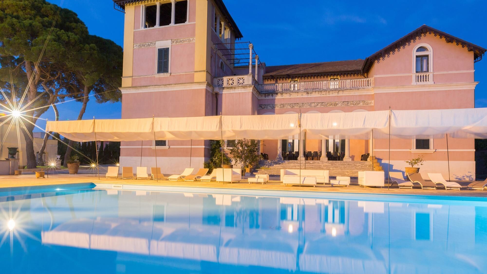 Un edificio spazioso con piscina, area salotto esterna e una scalinata che conduce all'ingresso.