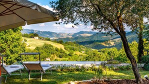Una terraza con una mesa y sillas, con vistas a un valle con colinas y una masa de agua.
