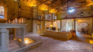Un interior amplio con chimenea de piedra, una zona de estar con sofá y sillones, y una mesa de comedor.