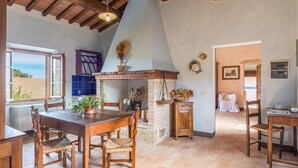 A rustic kitchen with a stone fireplace, wooden furniture, and a view of the outdoors. - Si-g602-pien0at - Podere Bagnolo 8 (Pienza)