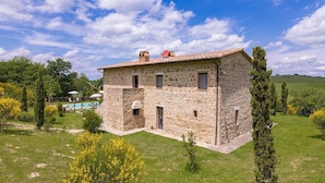 A stone house with a tiled roof, a swimming pool, and a garden with yellow flowers and cypress trees. - Si-g602-pien0at - Podere Bagnolo 8 (Pienza)